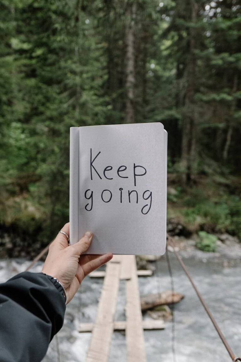 person holding a notebook with a text keep going on the background of a river in a forest