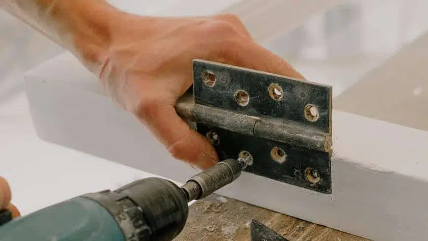 crop handyman fastening metal hinge on white window. God can fix your New Year in 2022.