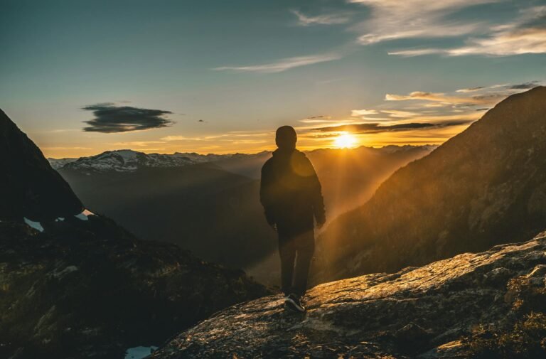 back view of a person standing in front of mountains during sunset