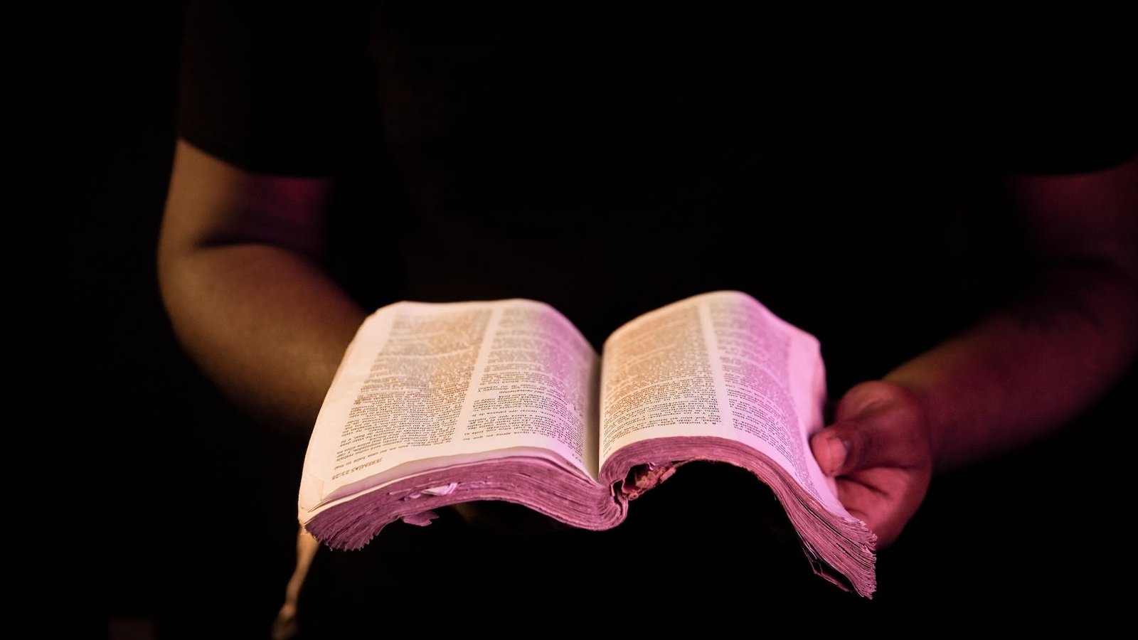 the person holding a bible with black background, praying for God to help him to manage his money well and to make wise choices.