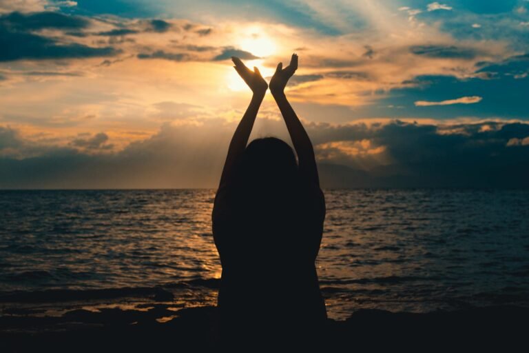 person raising hands near sea at sunset