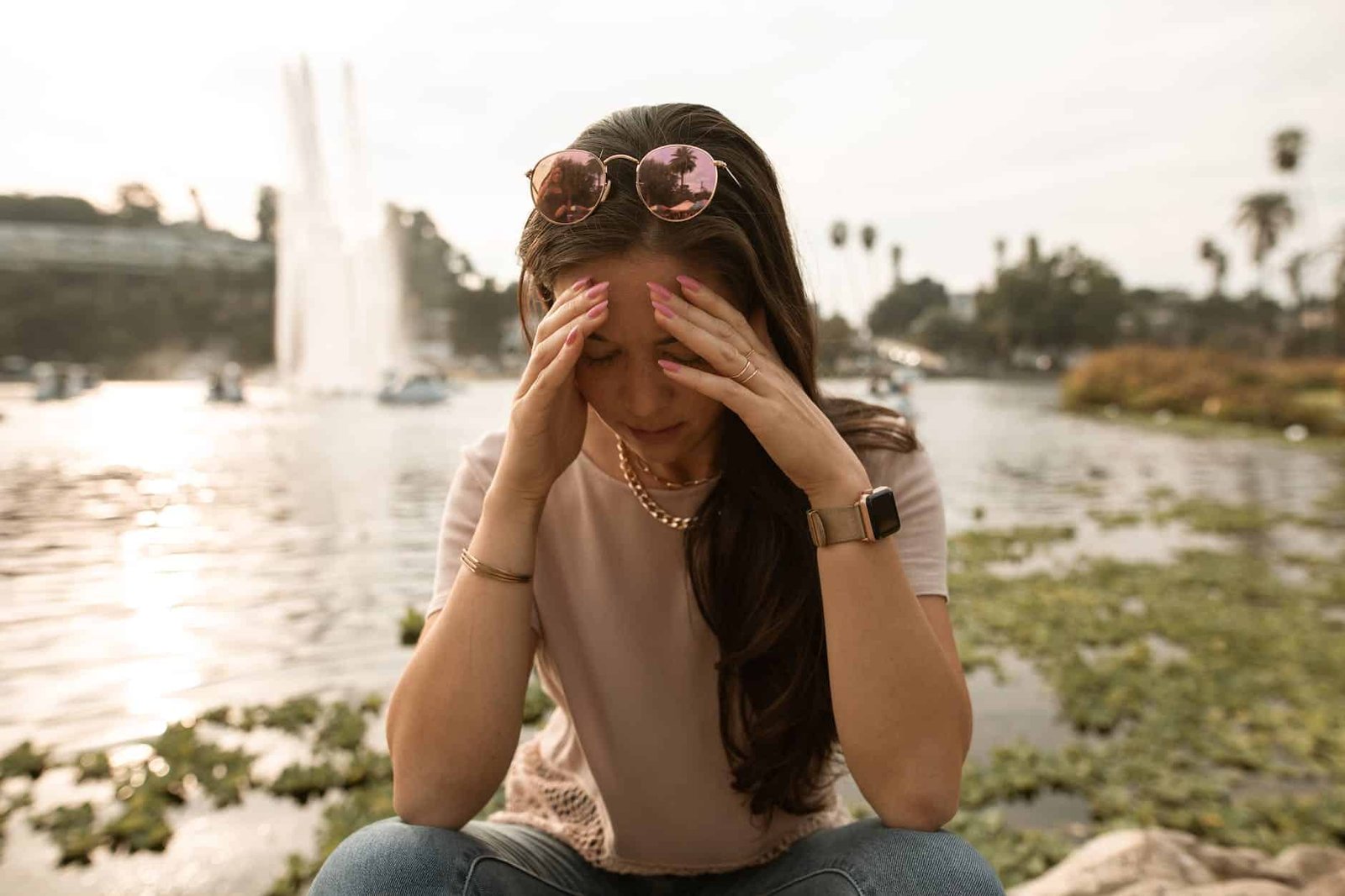 distressed woman sitting on lakeside and touching face in despair