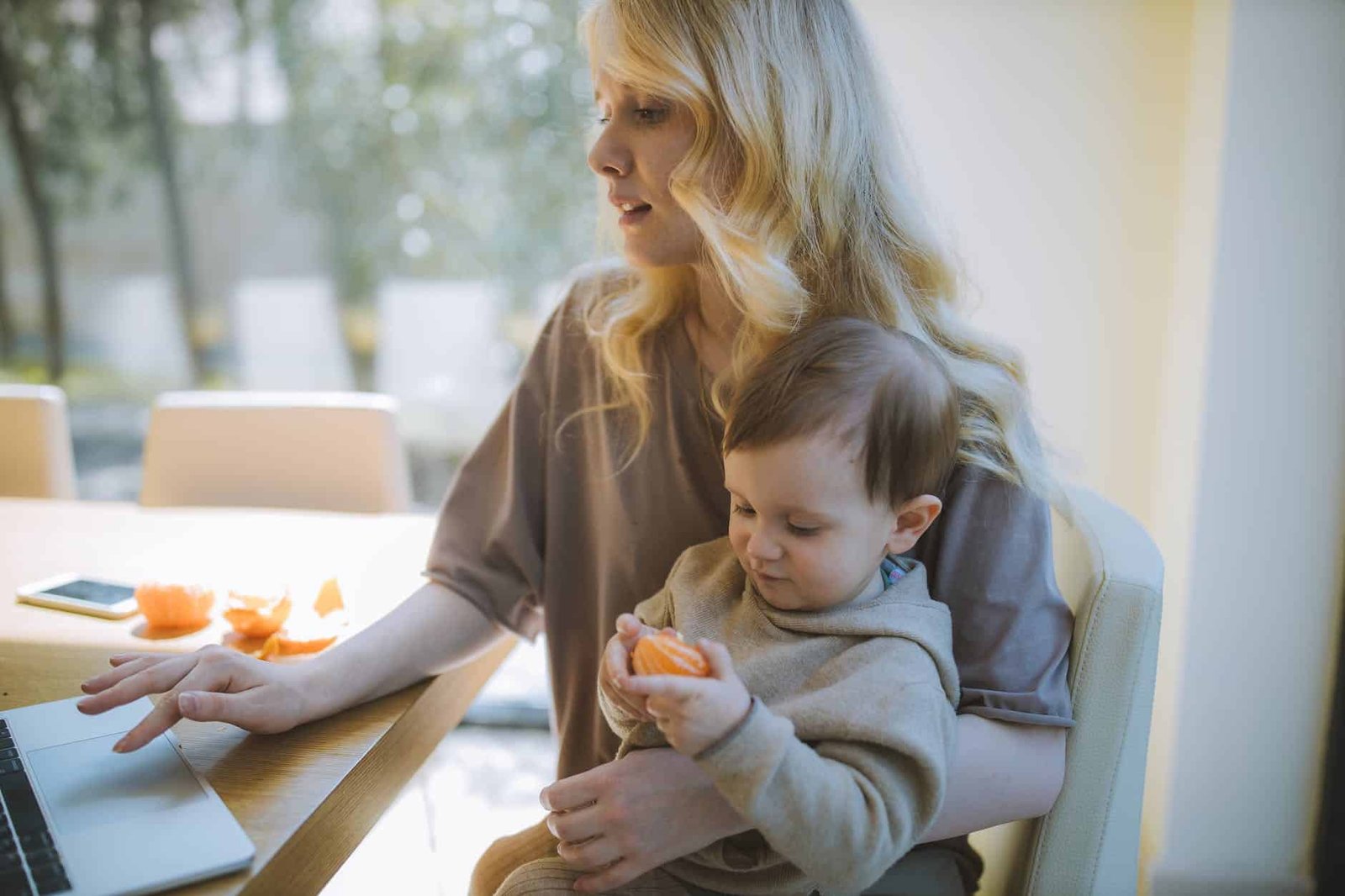 photo of woman carrying her baby while working on her laptop