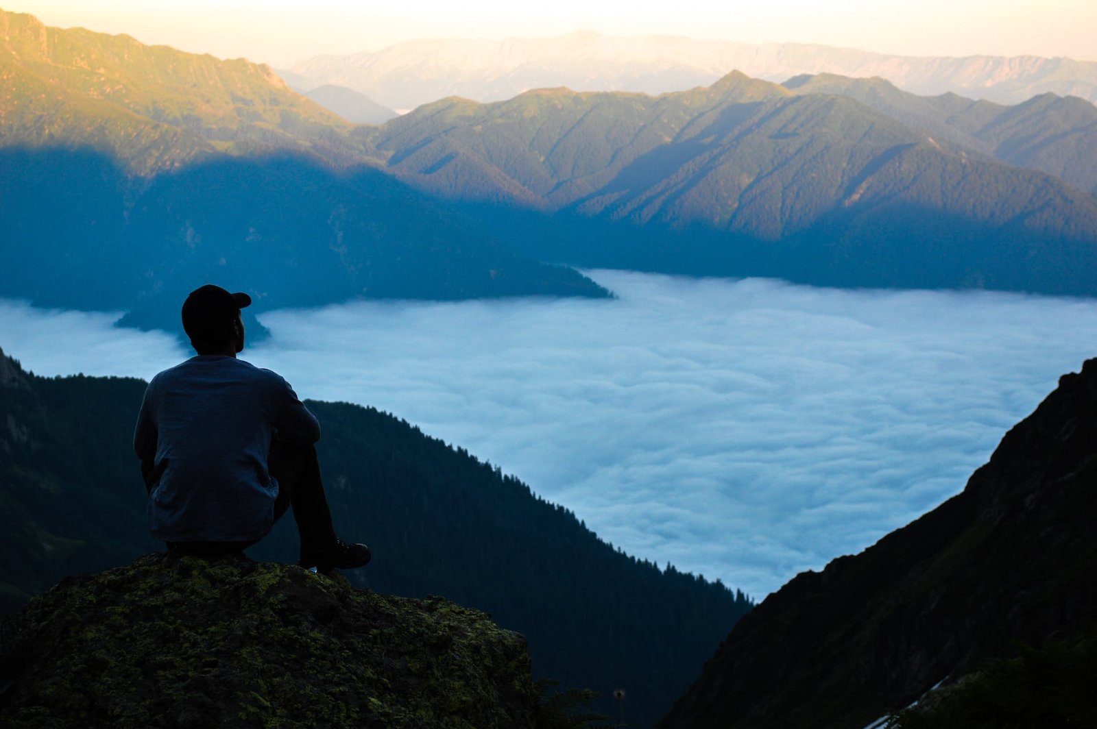 man on the edge of the cliff above the cloudy sky