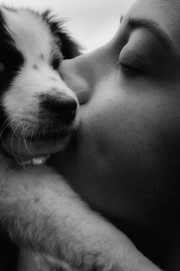 a black and white photo of a woman kissing a dog