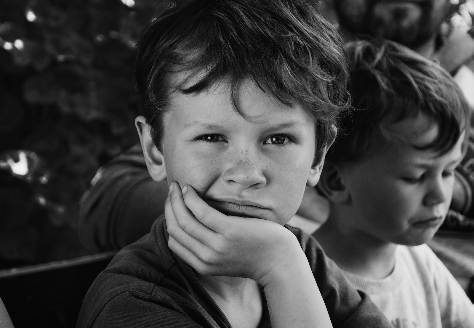 freckled boy with head rested on his hand sitting next to his little brother and father on a bench