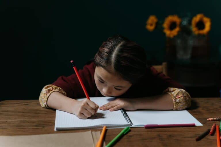 a girl writing on a notebook using a pencil