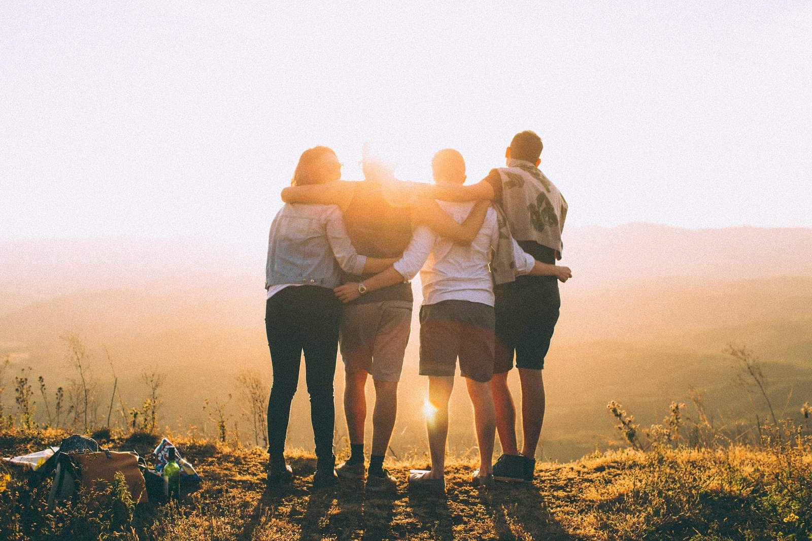 four person standing on cliff in front of sun