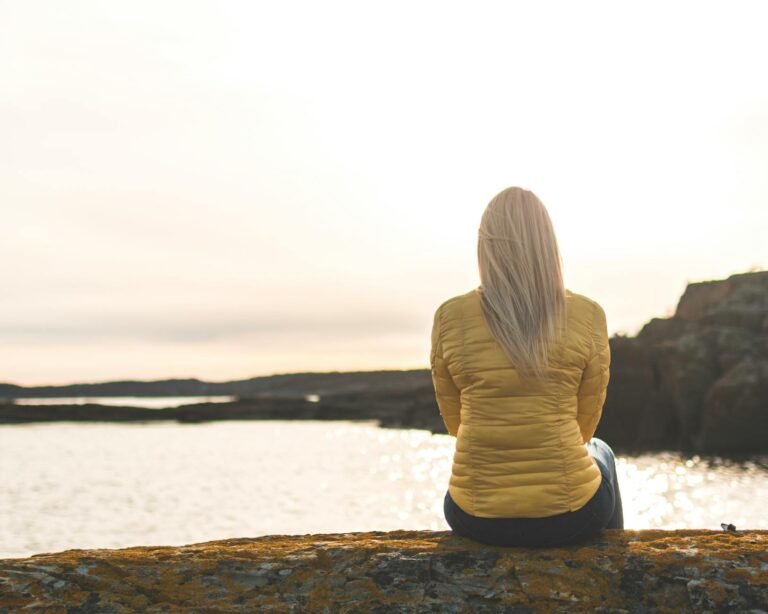 woman wearing yellow bubble jacket sitting in front of sea