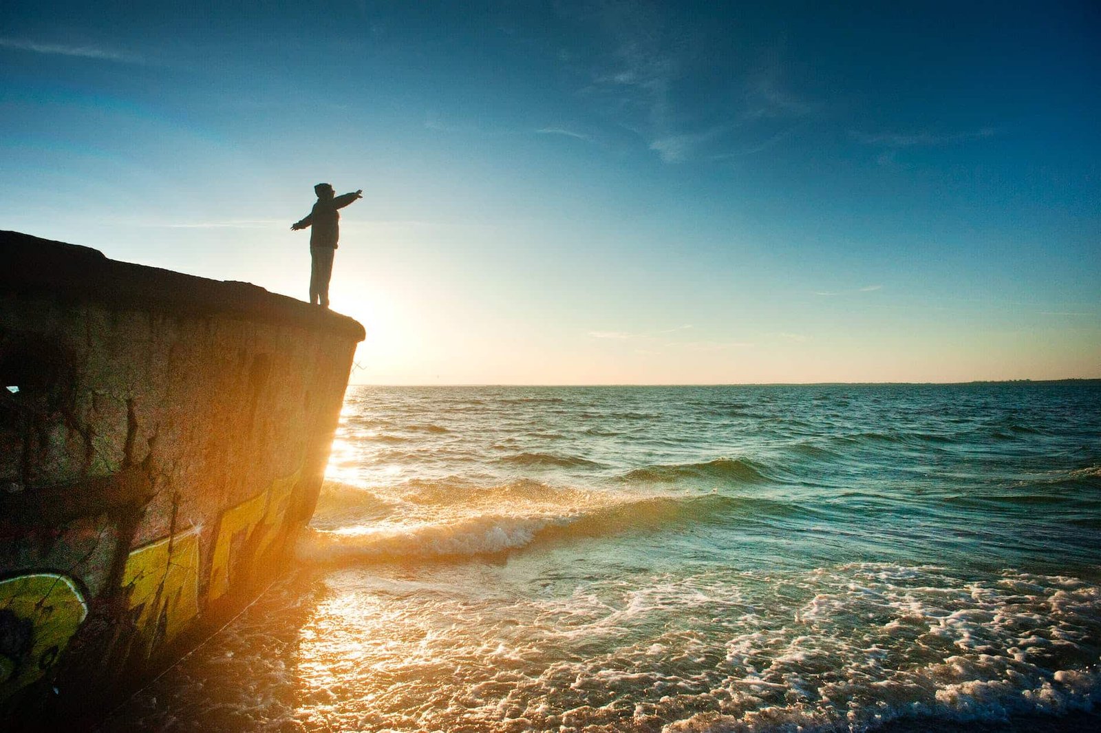 silhouette of person on cliff beside body of water during golden hour