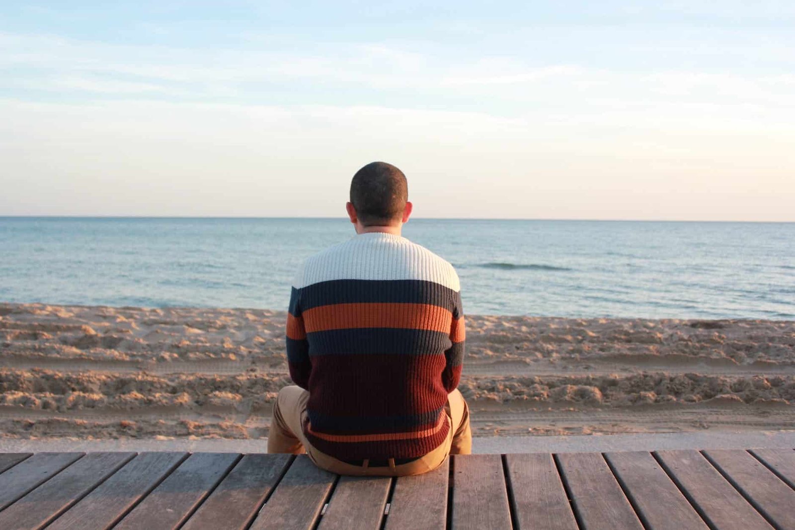 man sitting on wooden panel facing in the ocean