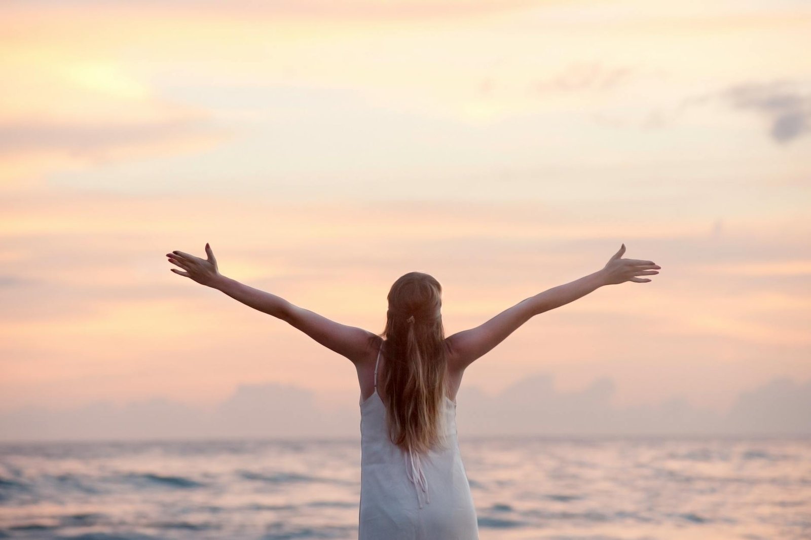 rear view of woman with arms raised at beach during sunset