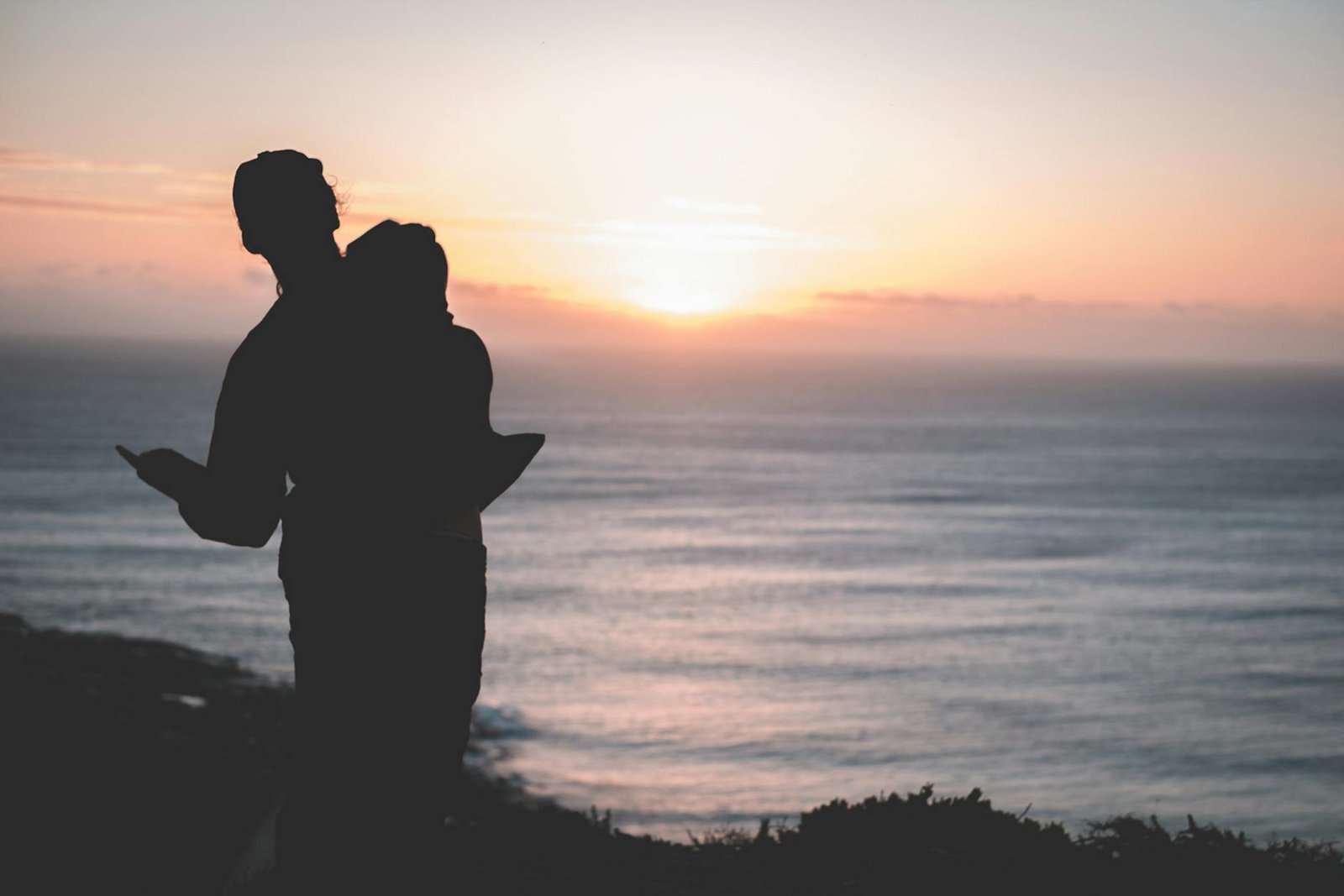 silhouette of couple standing on sea coast at sunset