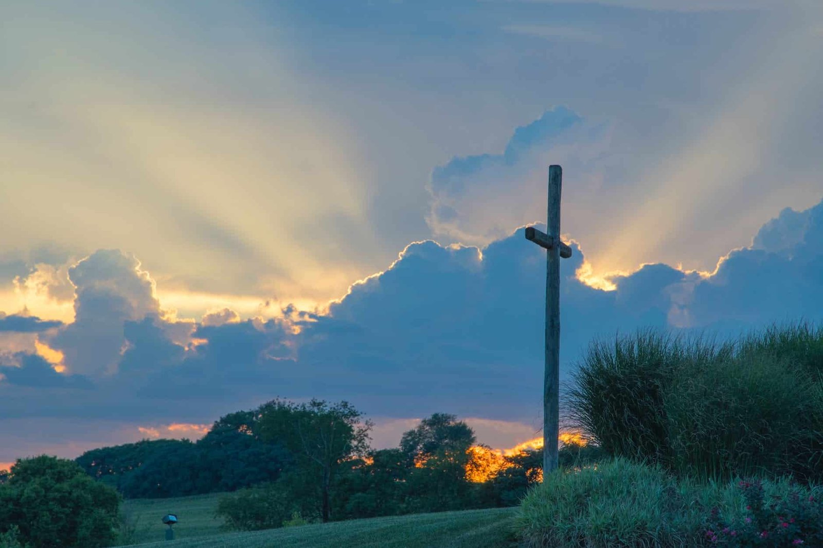 big wooden cross on green grass field under the white clouds