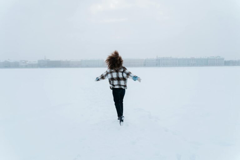 woman running through snow field with arms stretched out