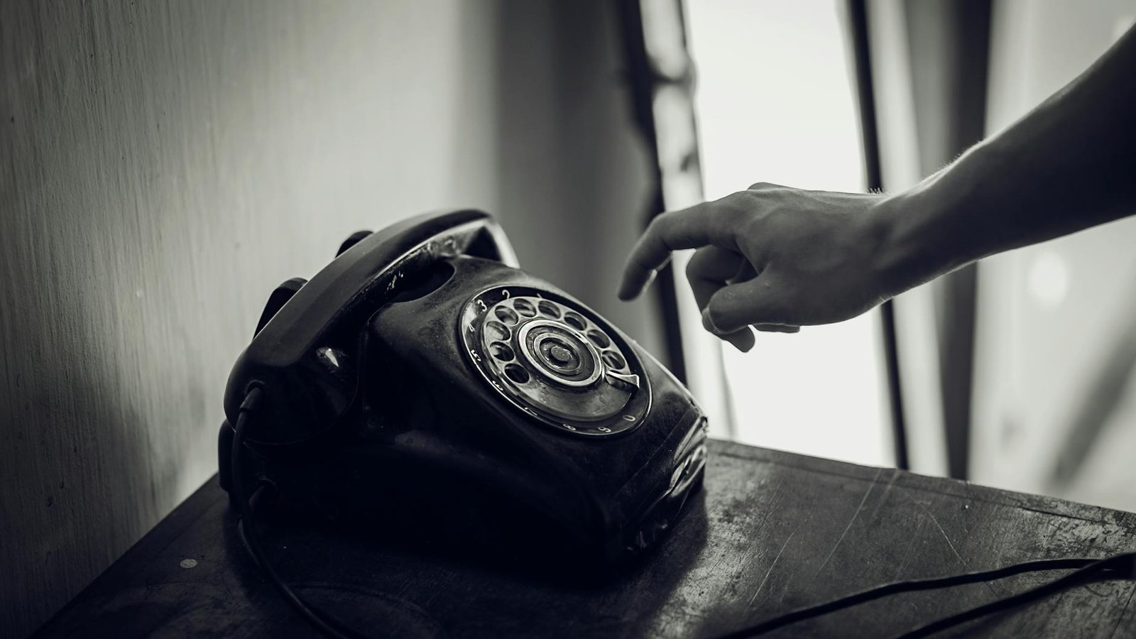 grayscale photo of rotary telephone beside person hand