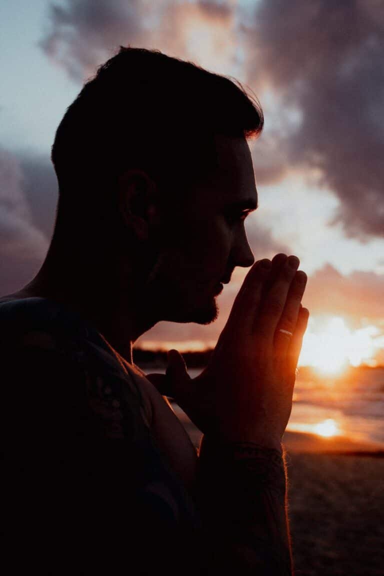 silhouette of a man with his hands in a prayer position at sunset