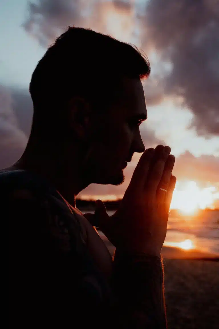 silhouette of a man with his hands in a prayer position at sunset